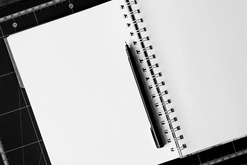 Open spiral notebook with a blank page and a black pen on a cutting mat