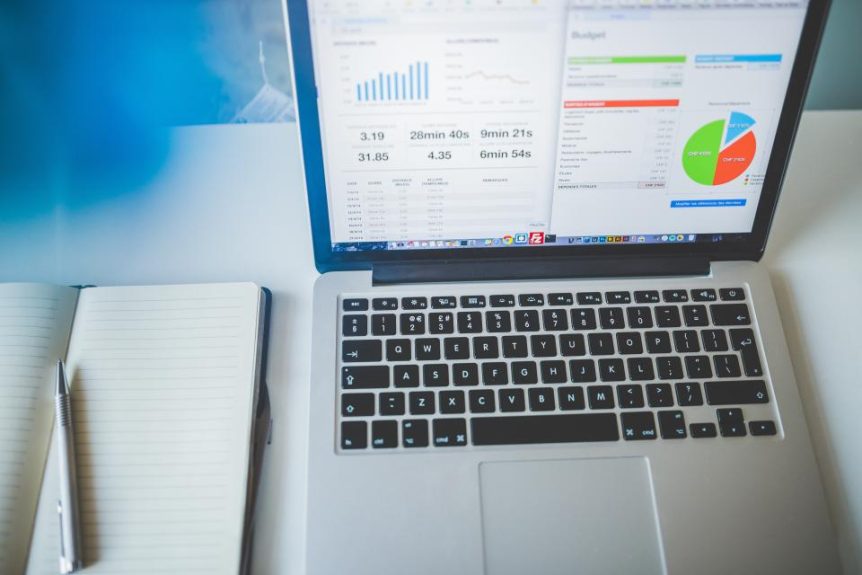 Laptop showing charts on a desk next to a notebook