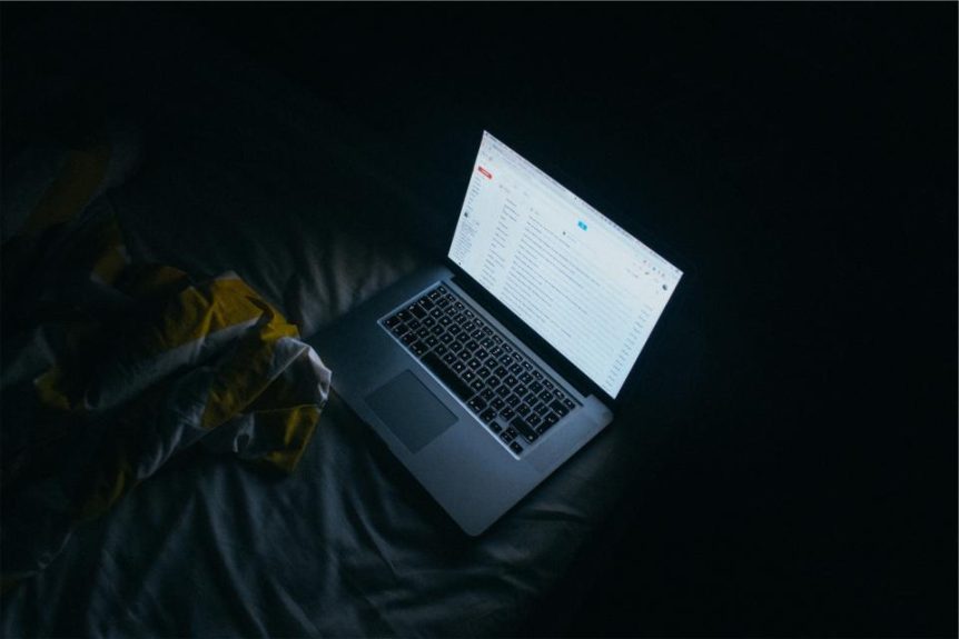 Open laptop showing an email inbox in a dark room