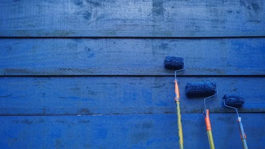 Three paint rollers leaning against a freshly painted blue wooden wall