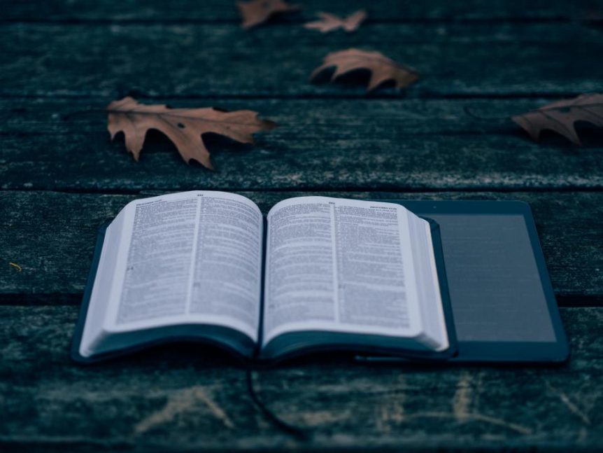 Open book beside a tablet on a wooden surface