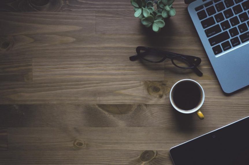 Cup of black coffee next to a laptop and glasses on a wooden desk