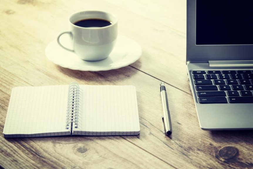 Coffee cup, open notebook, pen and laptop on a wooden table