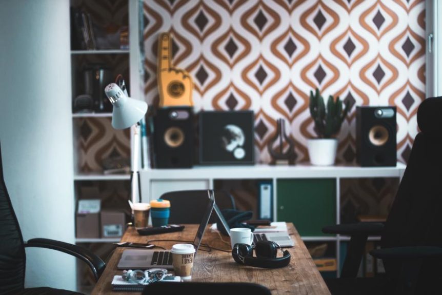 A creative home office with a laptop, desk lamp and patterned wallpaper