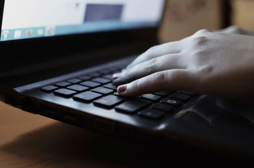 Close-up of a hand typing on a black laptop keyboard
