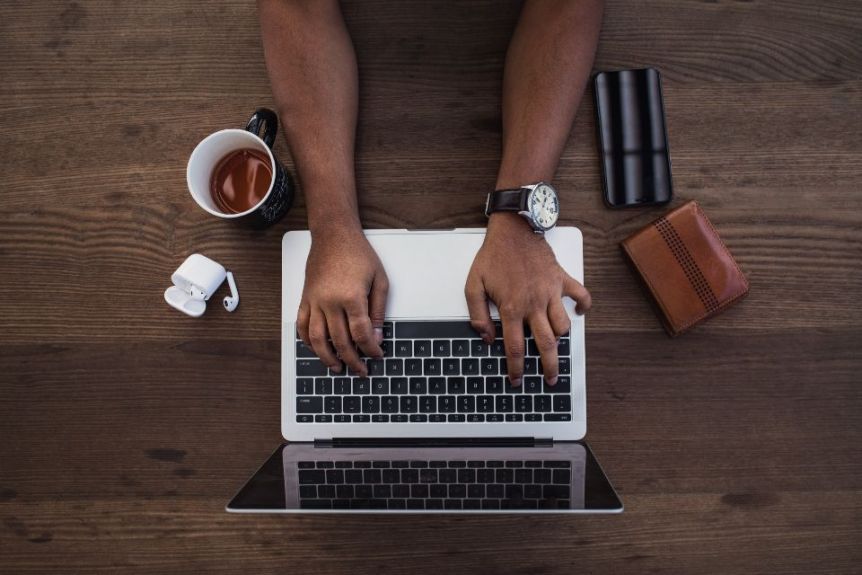 Hands typing on a laptop on a wooden desk, seen from above