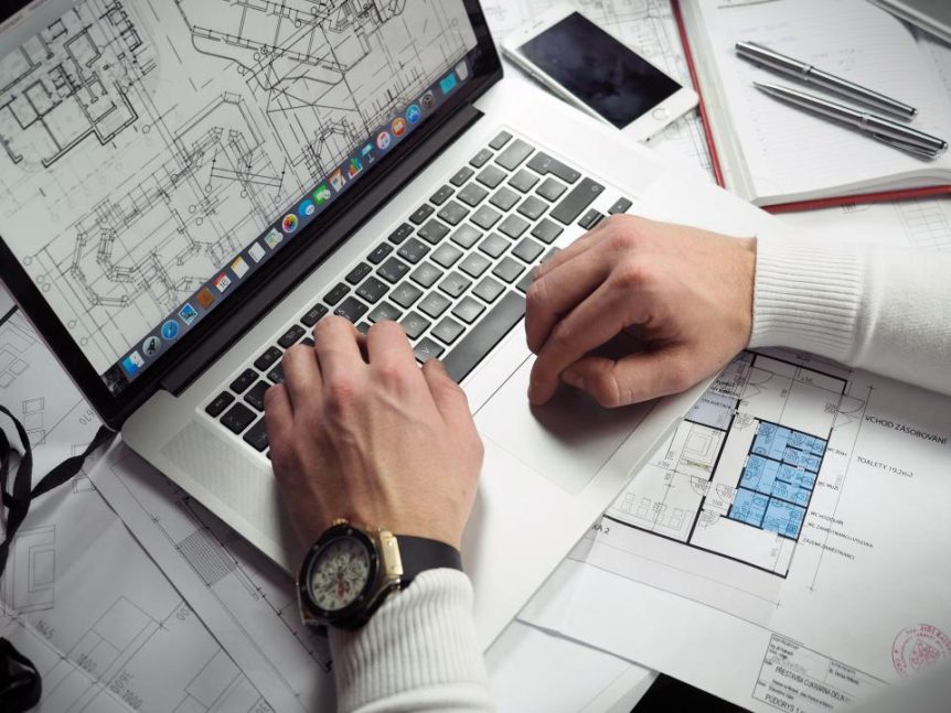 Hands typing on a laptop surrounded by design drawings