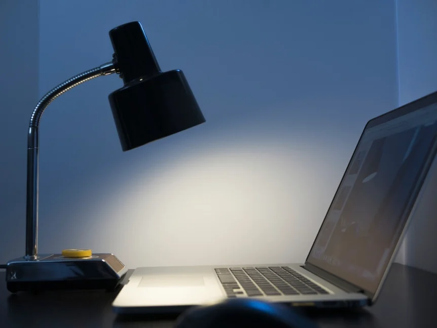 Laptop on a desk lit by a black desk lamp