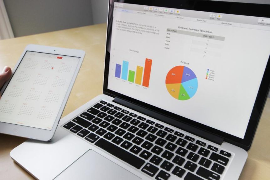 Laptop showing charts and a spreadsheet next to a tablet on a desk