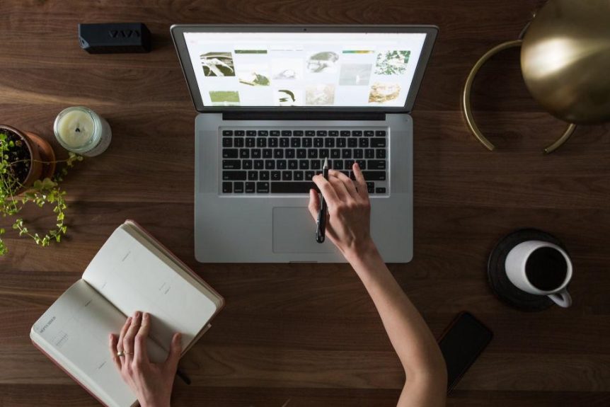 Laptop on a wooden desk with a notebook, coffee mug and plant