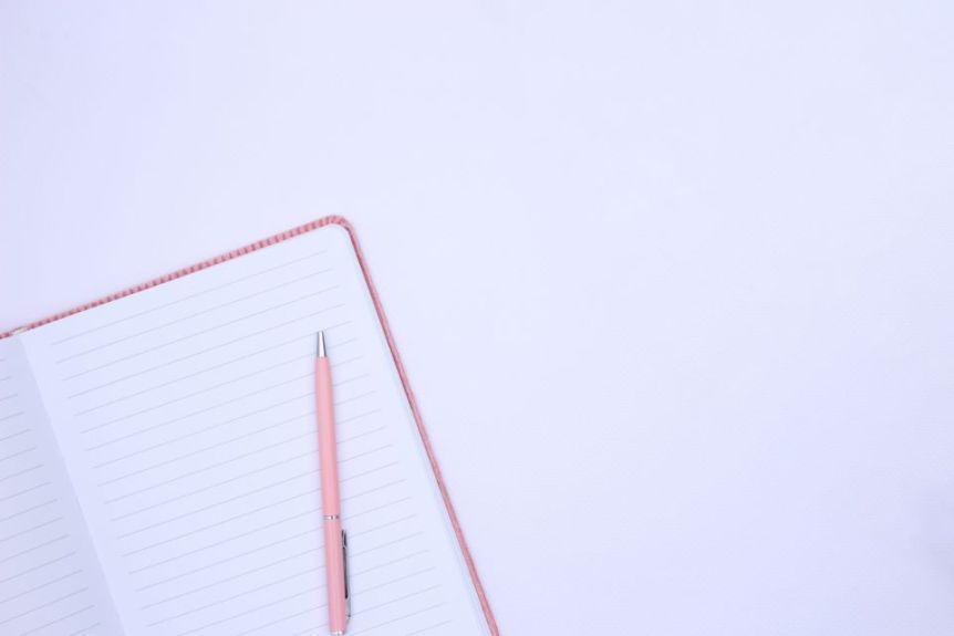 Open lined notebook with a pink pen on a pale background
