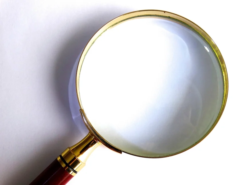 Brass magnifying glass with a red handle on a white surface