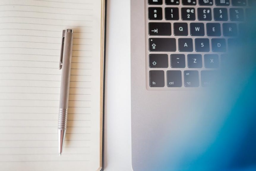 Notebook and pen next to a laptop keyboard