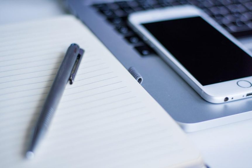 Pen on a notebook beside a smartphone and laptop
