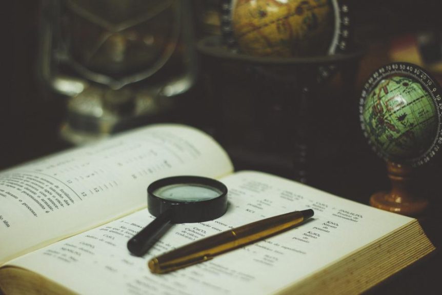 Open book with a magnifying glass and pen beside small desk globes