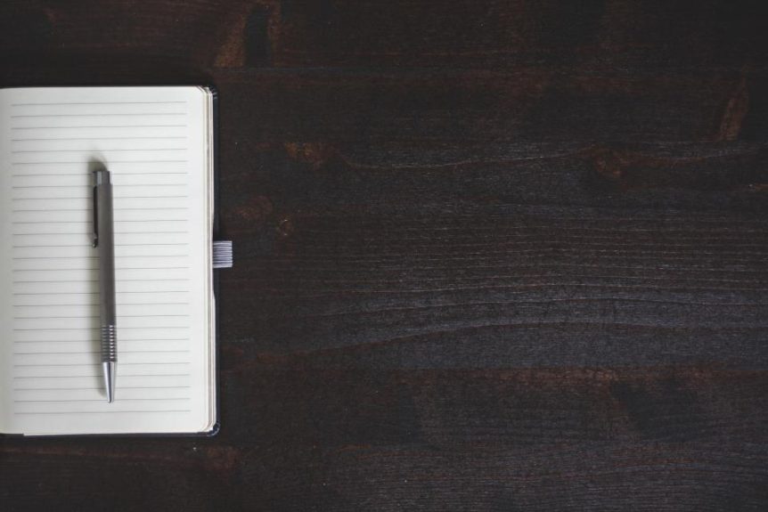 Open lined notebook with a pen on a dark wooden desk
