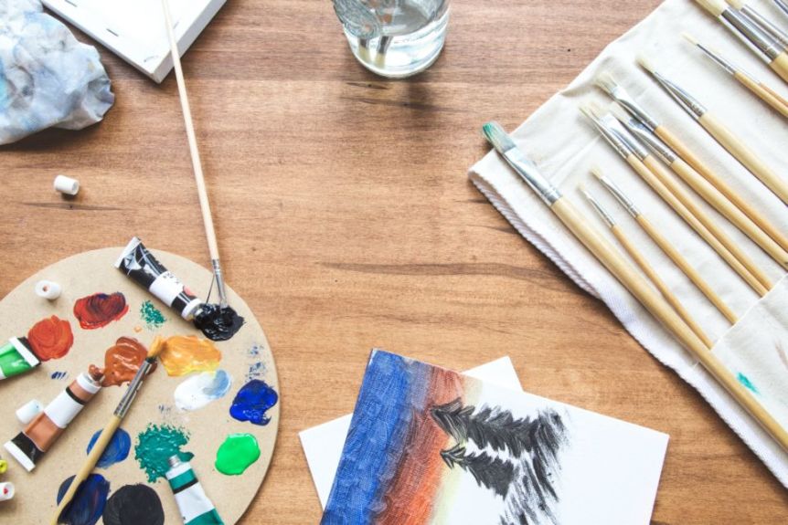 Paint palette, brushes and a small painting on a wooden table