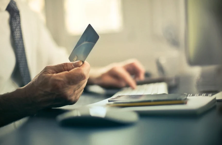 Hand holding a payment card at a computer desk