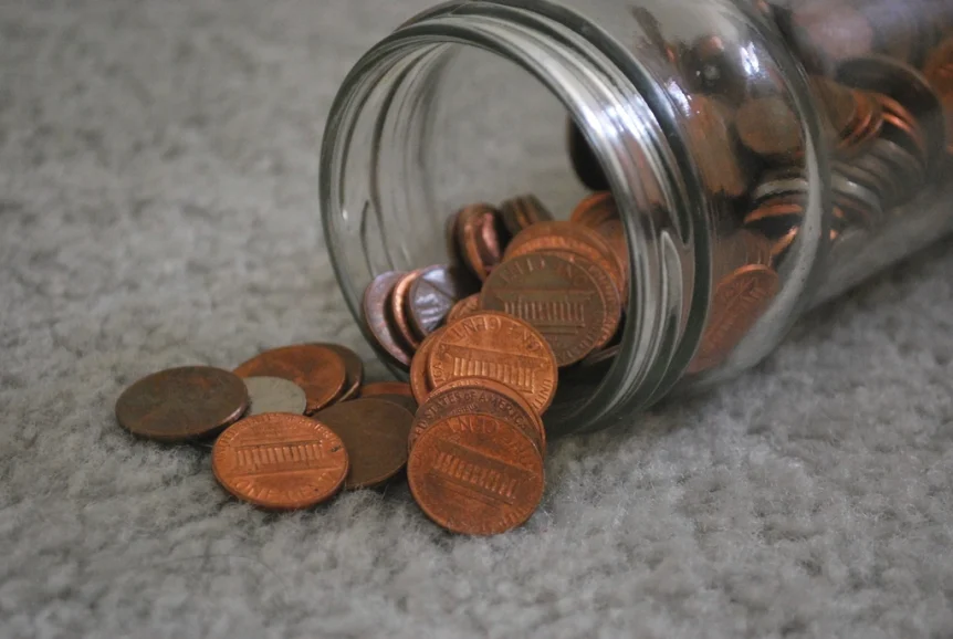 Pennies spilling out of a glass jar onto a carpet
