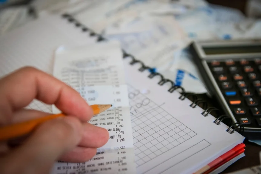 Hand with a pencil checking a receipt next to a notebook and calculator