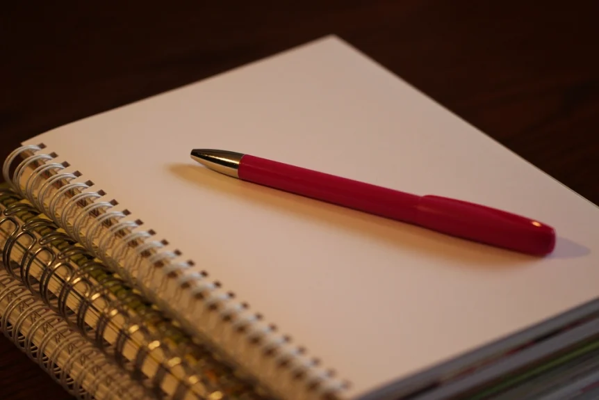 Red pen resting on a stack of blank spiral notebooks