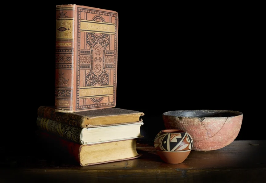 A small stack of old hardcover books beside a clay bowl on a dark wooden table