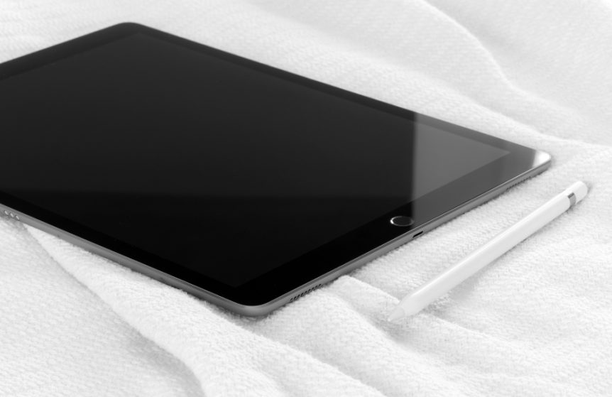 A tablet and stylus resting on a white blanket
