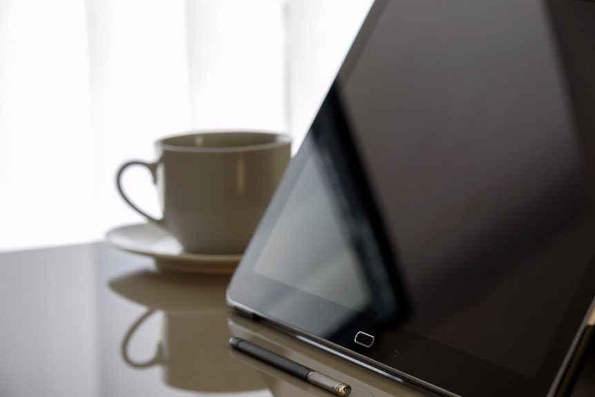 A tablet with a dark screen beside a white coffee cup