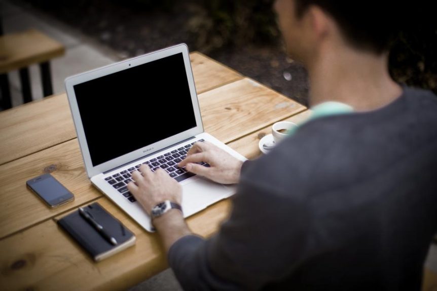 Person typing on a laptop at a wooden table